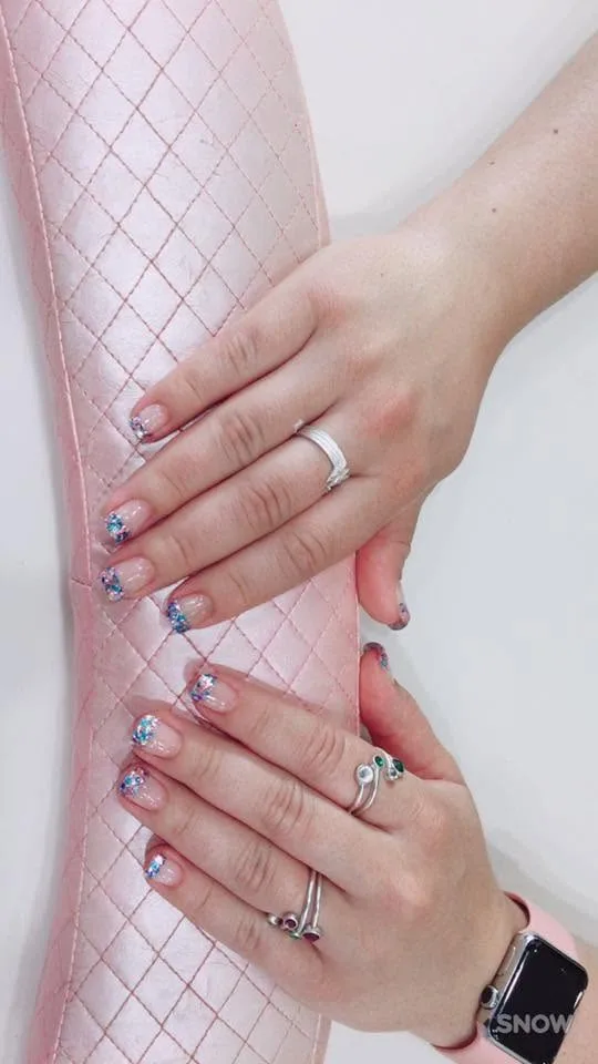 Longer nails on a clear base with blue and silver glitter swept up from the cuticle, resting on a pink quilted manicure cushion