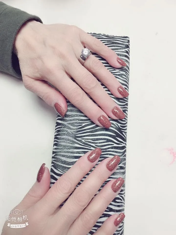 Long square nails in copper glitter gel, both hands resting on a zebra-print file on the manicure table